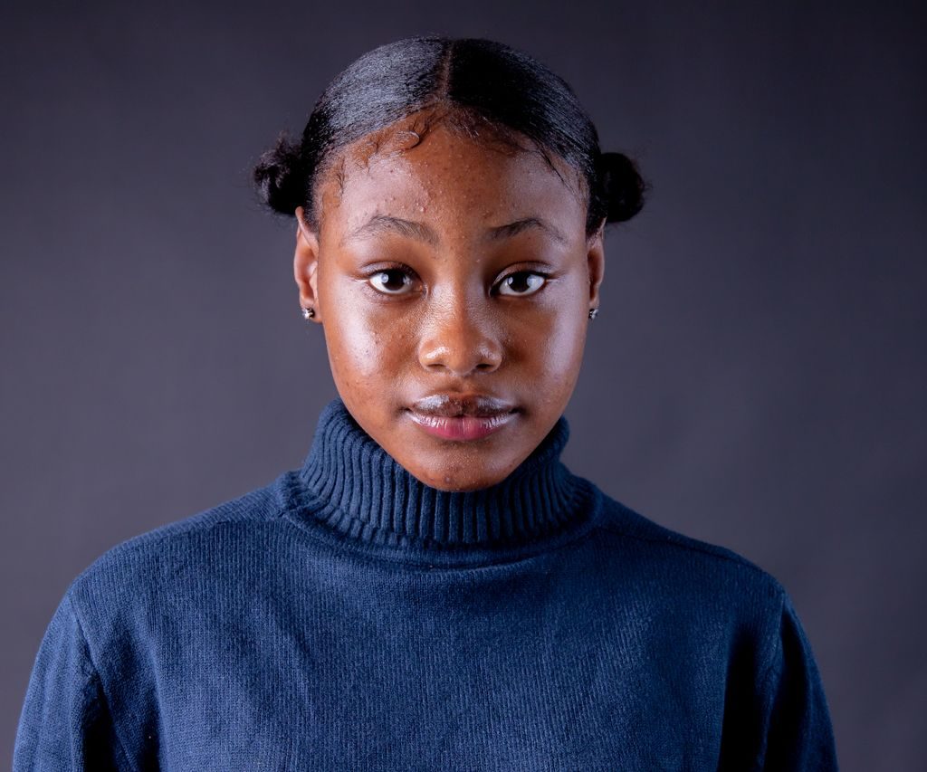 Elegant studio portrait of a young black woman wearing a blue turtleneck. Neutral background.